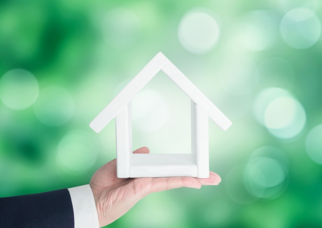 家の模型を持つビジネスマン 緑背景