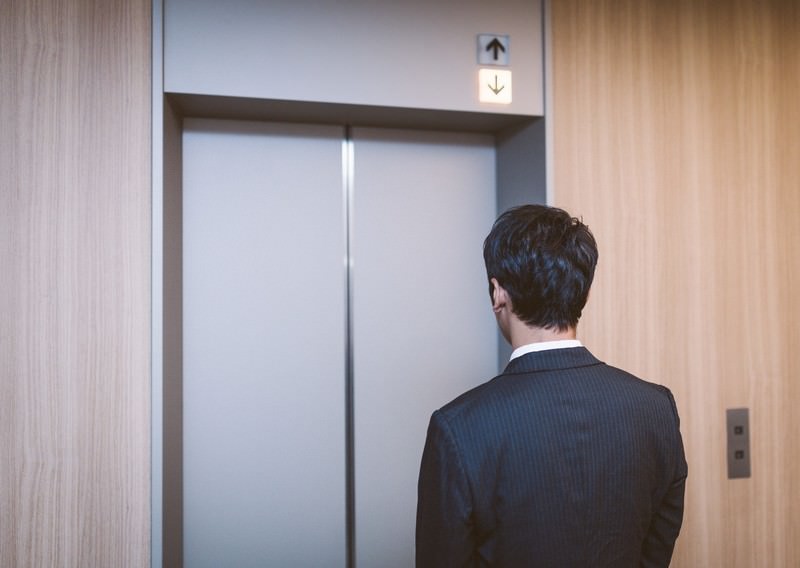 エレベーターを待つスーツ姿の男性、昇降表示を見つめる