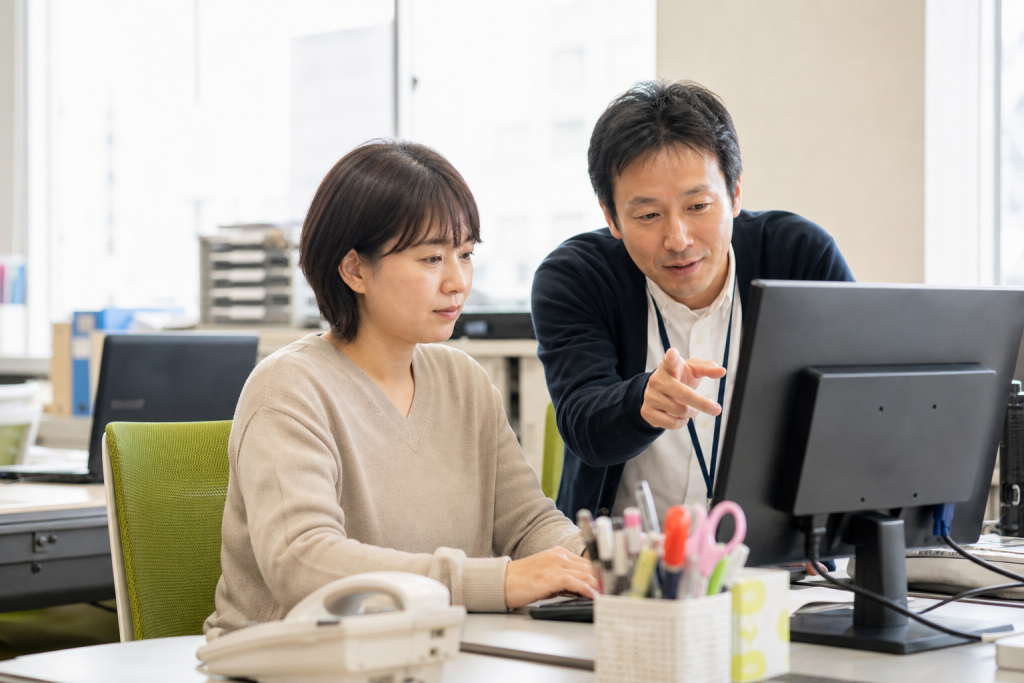 就労継続支援A型の事業所でパソコン業務に取り組み、支援員から説明を受ける利用者
